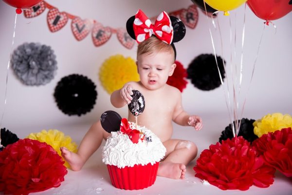 Bebê brincando com bolo em ensaio Smash the Cake com tema da Minnie, em cenário vermelho, amarelo e preto.