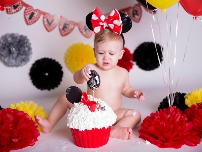 Bebê brincando com bolo em ensaio Smash the Cake com tema da Minnie, em cenário vermelho, amarelo e preto.
