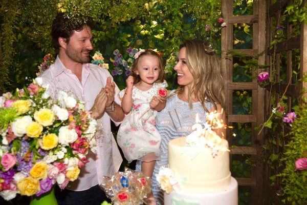Pais com a filha ao lado do bolo durante uma festa de aniversário infantil