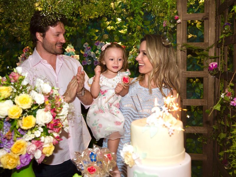 Pais com a filha ao lado do bolo durante uma festa de aniversário infantil